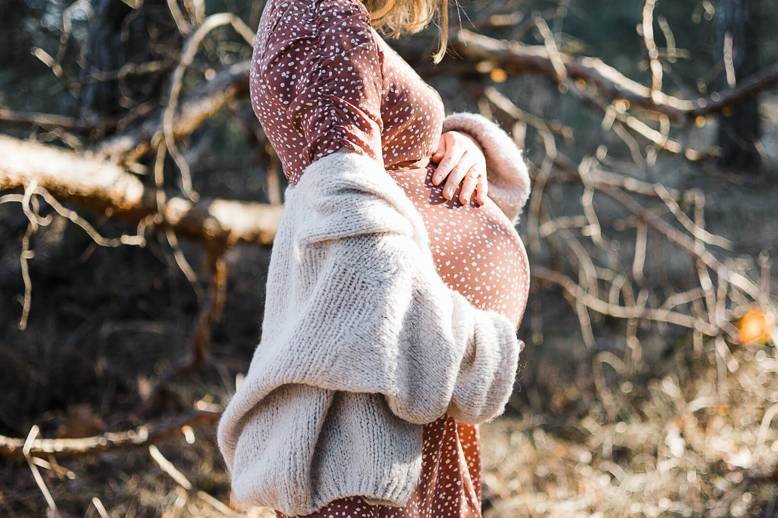 Eine schwangere Frau steht im Wald und zeigt ihren Babybauch