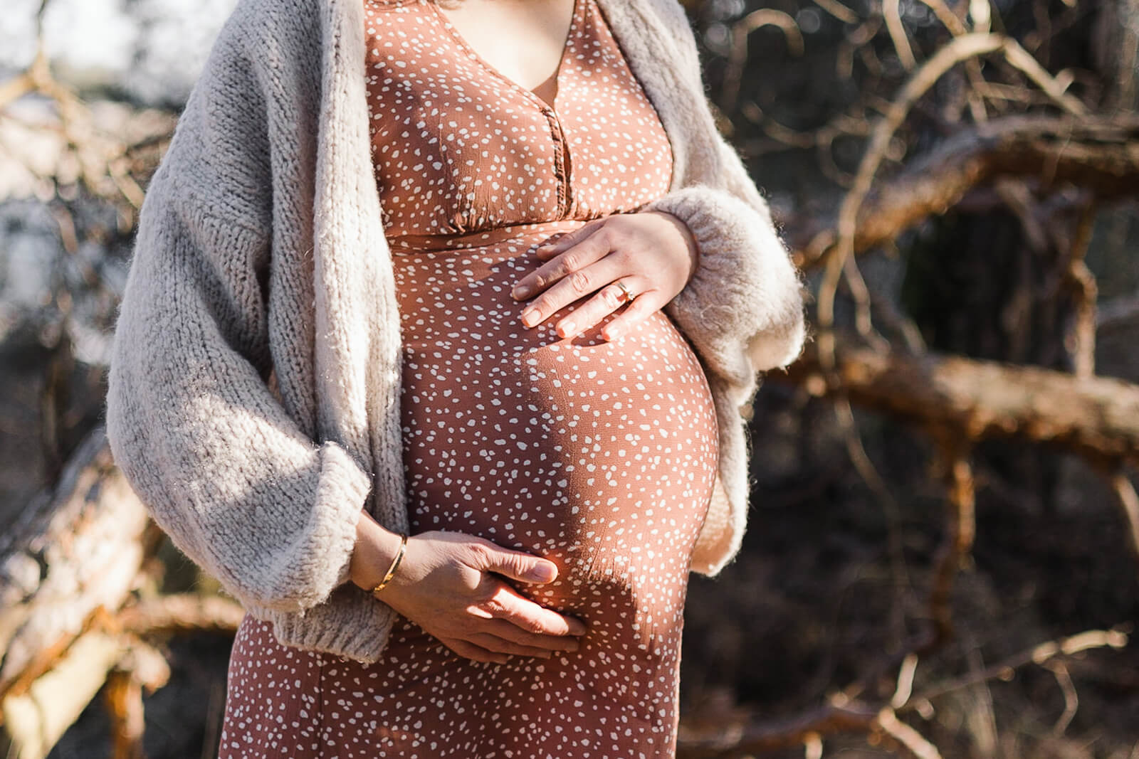 Eine schwangere Frau steht in der Wintersonne und zeigt ihren Babybauch