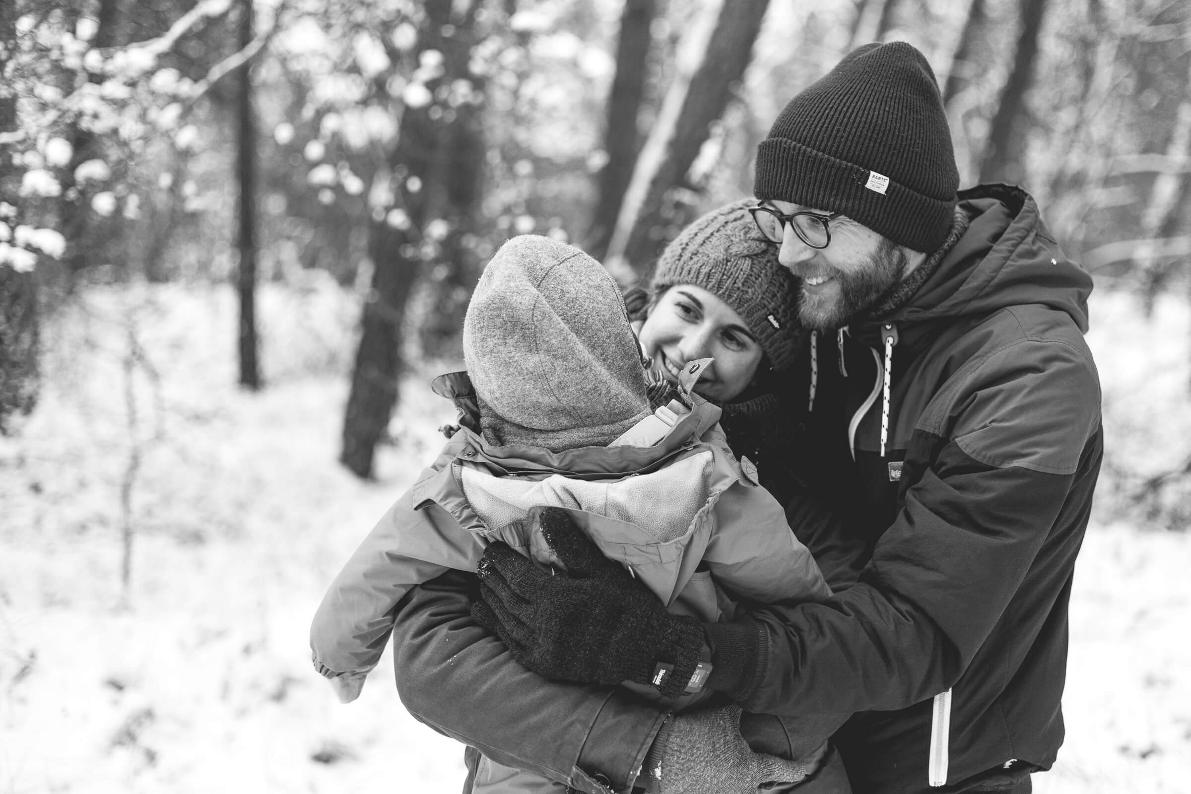 Eine kleine Familie mit einem Baby kuschelt sich an einem Wintertag im Schnee eng aneinander